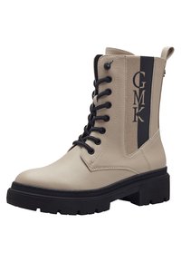 Bottes cheville en cuir beige avec quincaillerie noire, devant à lacets et un panneau latéral à motifs arborant le texte "GMK". Semelle noire épaisse pour plus de stabilité.