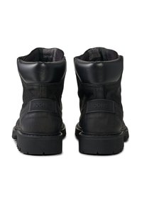 Schwarze Stiefeletten mit einer Kombination aus glattem und strukturiertem Leder, einer robusten Gummisohle und einem erhöhten Markenlogo auf der Rückseite.