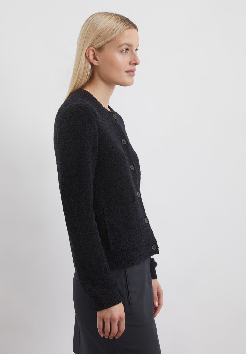 Schwarze, strukturierte Strickjacke mit rundem Ausschnitt, Knopfverschluss, langen Ärmeln und aufgesetzten Taschen vorne.