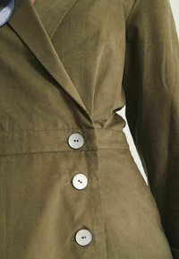 Veste en velours côtelé vert olive au design ajusté, dotée de boutons en métal argenté et d'un col à revers, mettant en avant une texture à côtes verticales.