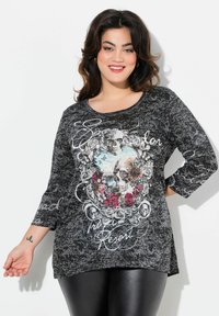 Schwarzes T-Shirt mit Rundhalsausschnitt und Dreiviertelärmeln, das ein florales Totenkopfdesign und weißen Schrifttext zeigt, hergestellt aus strukturiertem Material.