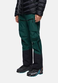 Groene technische broek met zwarte onderbenen, meerdere ritszakken en een slim fit ontwerp. Gecombineerd met zwarte laarzen met blauwe accenten.
