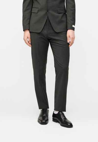 Σκούρο γκρι κοστούμι με εφαρμοστή σακάκι και παντελόνι με επίπεδη μπάρα. Ζευγάρι μαύρα δερμάτινα παπούτσια, λεία υφή, ελάχιστες λεπτομέρειες.