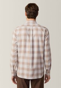 Camisa a cuadros marrón y blanco con mangas largas y puños con botones, que presenta un detalle de canesú en la parte trasera. Tejido de algodón ligero.