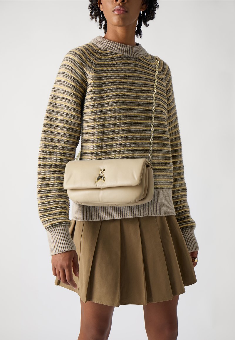 Borsa a tracolla in pelle beige con dettagli in hardware dorato e catenina, abbinata a un maglione a righe e a una gonnellina plissettata marrone.