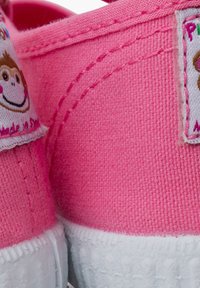 Pink canvas shoes with white rubber soles, featuring labels with a monkey design and "Made in Spain" text. Closed-toe design.
