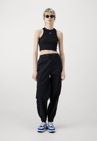 Black crop tank top with round neckline and blue logo; black cargo pants with elastic cuffs and drawstring waist; blue and white sneakers.