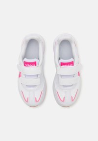 Białe buty sportowe z rzepami, z różowymi akcentami i brandingiem na języku, posiadające siateczkowe wnętrze i gumową podeszwę.