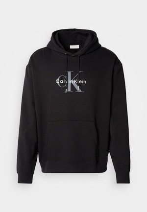 Crna dukserica s kapuljačom od pamuka, s prednjim džepom i otisnutim Calvin Klein logotipom u sivoj i bijeloj boji na prsima.