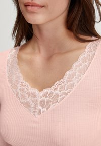 Pink ribbed top featuring a V-neckline adorned with delicate lace trim, showcasing a soft texture and subtle elegance.