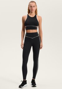 Čierny športový crop top s bielymi akcentmi a legíny s vysokým pásom so kontrastnými švami; doplnené čiernymi športovými topánkami.