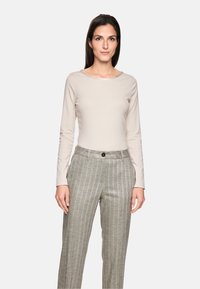 Beige Langarmoberteil aus glattem Stoff, kombiniert mit grauen, gestreiften Hosen mit Knopfverschluss und einer lässigen Passform.