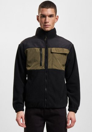Fleece jacket in black and olive green. Features a high collar, zippered chest pocket, and elastic cuffs for comfort. Soft texture.