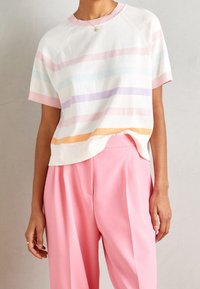 Suéter de manga corta en blanco con patrones de rayas en tonos pastel; presenta un escote redondo y dobladillo acanalado; combinado con pantalones de pierna ancha en rosa.