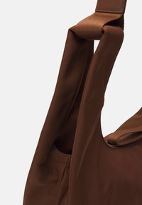 Sac fourre-tout en tissu marron avec une texture lisse et des poignées larges. Doté d'une poche latérale et de coutures propres pour plus de durabilité.