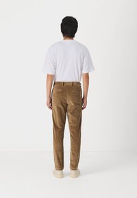 Pantaloni di velluto a coste marroni con taglio dritto, abbinati a una semplice t-shirt bianca. L'outfit è completato da calzature di colore chiaro.