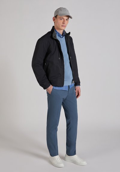 Men's outfit featuring a black jacket, light blue sweater, blue striped shirt, blue trousers, and white sneakers, with a light gray cap.