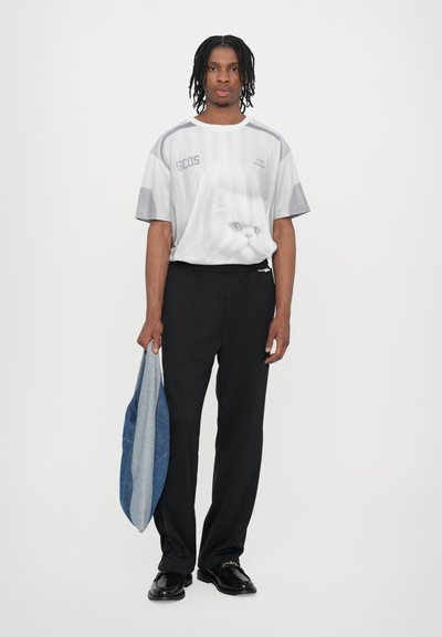 Grå grafisk t-shirt med et katte-design, sorte bukser og en lyseblå taske. T-shirten har en rund halsudskæring og korte ærmer.