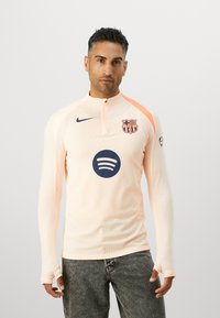 Light peach long-sleeve athletic top with ribbed texture, half-zip collar, Barcelona logo, and Spotify graphic on the front.