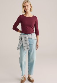 Bordowa bluzka z długim rękawem zestawiona z jasnoniebieskimi dżinsami. Jasnoszary sweter w paski zawiązany w talii. Brązowe trampki dopełniają strój.