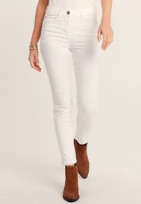 Witte skinny jeans met een gladde textuur, vijf zakken design en een voorste knoopsluiting, gecombineerd met bruine suede enkellaarsjes.