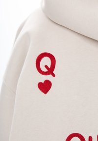 Felpa beige con ricamo rosso a forma di "Q" e cuore, con una texture liscia e un fit rilassato.