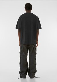 Schwarzes, oversized T-Shirt mit einem runden Ausschnitt, kombiniert mit Cargo-Hosen, die über seitliche Taschen und verstellbare Knöchelbündchen in einer passenden dunklen Farbe verfügen.