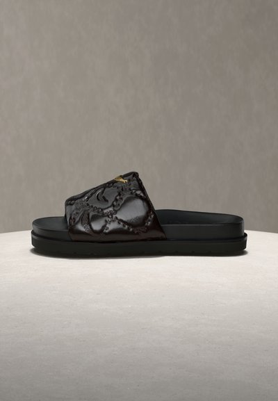 Μαύρη σαγιονάρα με ανάγλυφο floral μοτίβο και χρυσή λεπτομέρεια στον φαρδύ επάνω ιμάντα, επίπεδη σόλα, παρουσιάζεται σε ουδέτερη επιφάνεια.