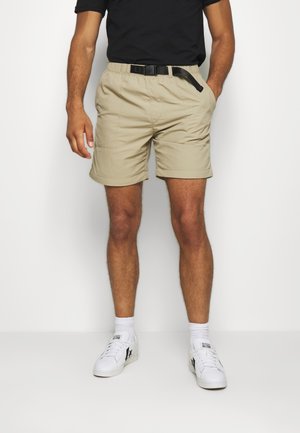 Beżowe szorty z elastycznym paskiem i czarnym paskiem, posiadające boczne kieszenie i klasyczny krój, zestawione z białymi sneakersami i skarpetkami.