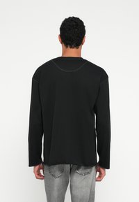 Juoda ilgomis rankovėmis palaidinė su apvalia iškirpte ir kontrastinga siūle. Audinys yra lygus, su laisvo kirpimo ir tiesia apačia.