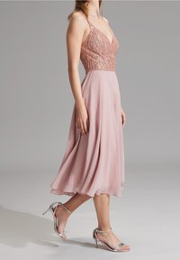 Sukienka bez rękawów, w dekolcie w serek, z dopasowanym, cekinowym gorsetem w kolorze różowego złota, prowadząca do zwiewnej, pastelowej różowej spódnicy z szyfonu. Zestawiona z srebrnymi szpilkami.