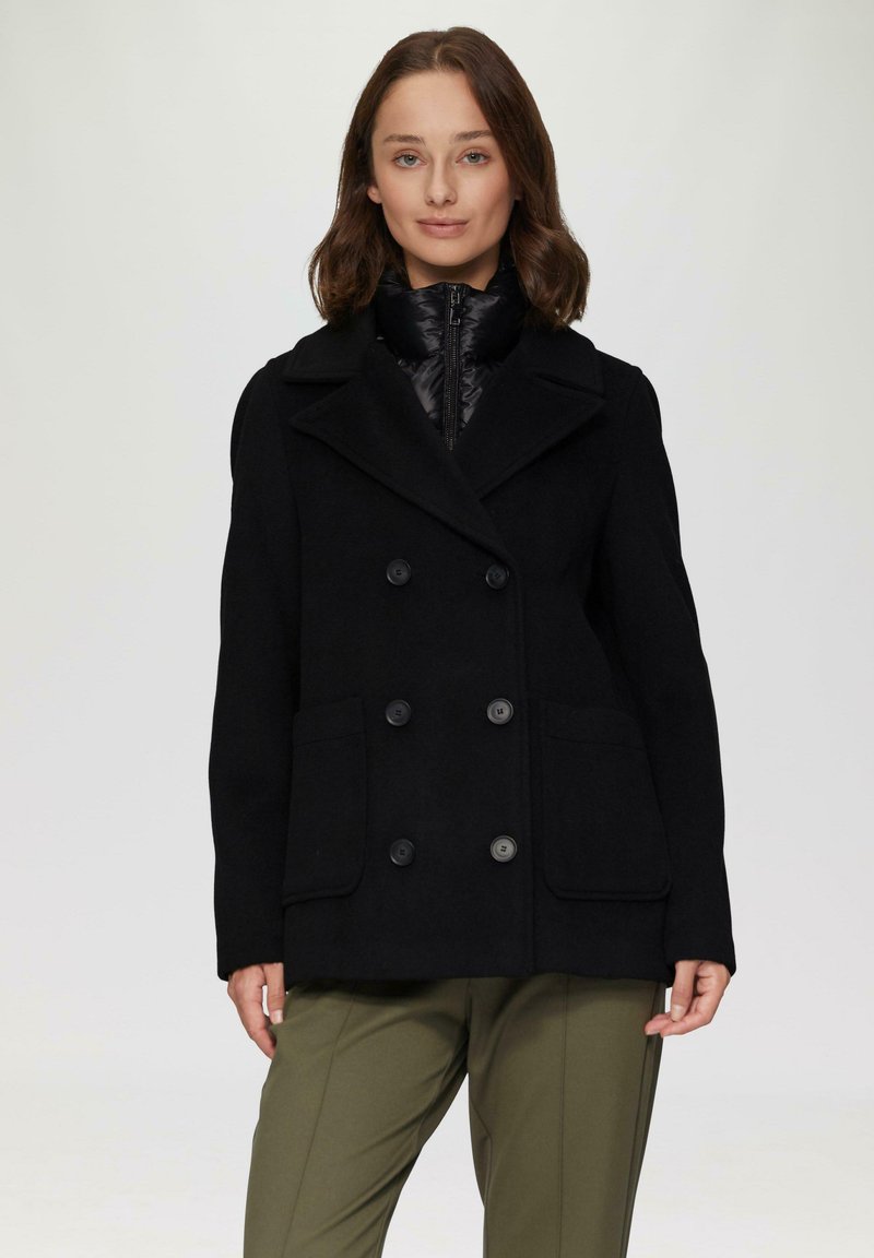 Schwarzer Wollmischung-Peacoat mit doppelreihigen Knöpfen, breitem Revers und zwei Fronttaschen, getragen über einer schwarzen gepolsterten Innenjacke.
