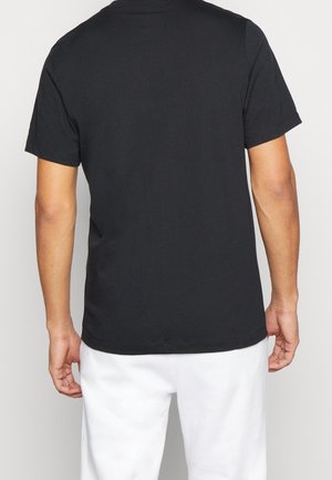 Mand iført ensfarvet sort t-shirt med korte ærmer og hvide bukser, set fra ryggen fra skuldrene til midt på lårene.