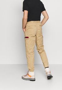 Beżowe spodnie cargo z elastycznym pasem, kieszeniami po bokach oraz tylną kieszenią z naszywką "NEW JEANS". Zestawione z wysokimi butami.