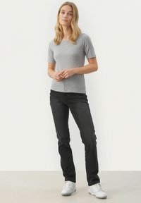Grå kortærmet t-shirt med rund halsudskæring, parret med sorte slim-fit jeans og hvide sneakers på en neutral baggrund.