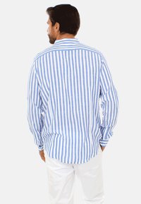Camicia a maniche lunghe a righe in lino azzurro chiaro e bianco, con colletto button-down e orlo arrotondato. La vista posteriore mostra un fit rilassato.