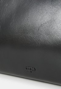 Gros plan sur une surface de cuir noir texturé avec un petit logo en relief près du bord inférieur.
