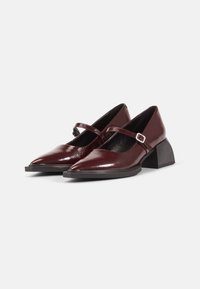 Burgundy patent leather heels with a pointed toe, cross strap, and block heel design. Smooth texture with a polished finish.