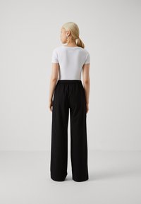 Haut blanc à manches courtes associé �à un pantalon large noir. Le pantalon a une taille élastique et une texture lisse. Design simple.
