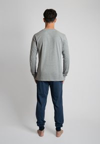 Grijze top met lange mouwen en een rechte snit, gecombineerd met marineblauwe jogpants met omgeslagen randen en een gestructureerde afwerking.