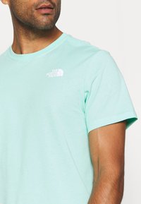 Krátké tričko světle zelené barvy z měkké bavlněné tkaniny, s bílým logem na levé straně hrudi a kulatým výstřihem.