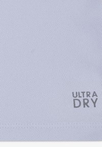 Ανοιχτό μπλε υφασμάτινο με υφή, με την επιγραφή «ULTRA DRY» σε γκρι χρώμα. Το υλικό φαίνεται διαπνέον και κατάλληλο για ρούχα που απομακρύνουν την υγρασία.