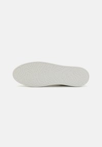 Hvit sneakersåle med et teksturert mønster som har bølgede linjer og en glatt kant. Merkets navn er preget nær hælen.