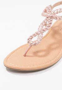 Tanssandali thong punane kuldne paelaga, millel on lame nahkpruun talla, sile, tekstureeritud pind ja minimalistlik disain.