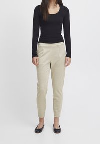 Schwarzes Langarmoberteil kombiniert mit beigen karierten, taillierten Hosen. Die Hosen haben eine mittelhohe Taille und Seitentaschen. Schwarze flache Schuhe.