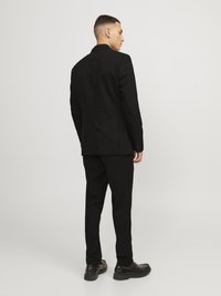 Black suit with a tailored fit, straight-cut trousers, and a notch lapel jacket. Shoes have a smooth leather finish and thicker sole.