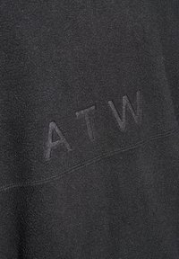 Pull en tissu noir avec une texture douce et mate, arborant un logo "ATW" en relief. Design simple, sans motifs ni éléments en métal visibles.