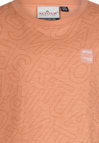 T-shirt color pesca realizzato in tessuto morbido con stampa tonale "RETOUR" e un piccolo logo sulla parte sinistra del petto. Collo rotondo.