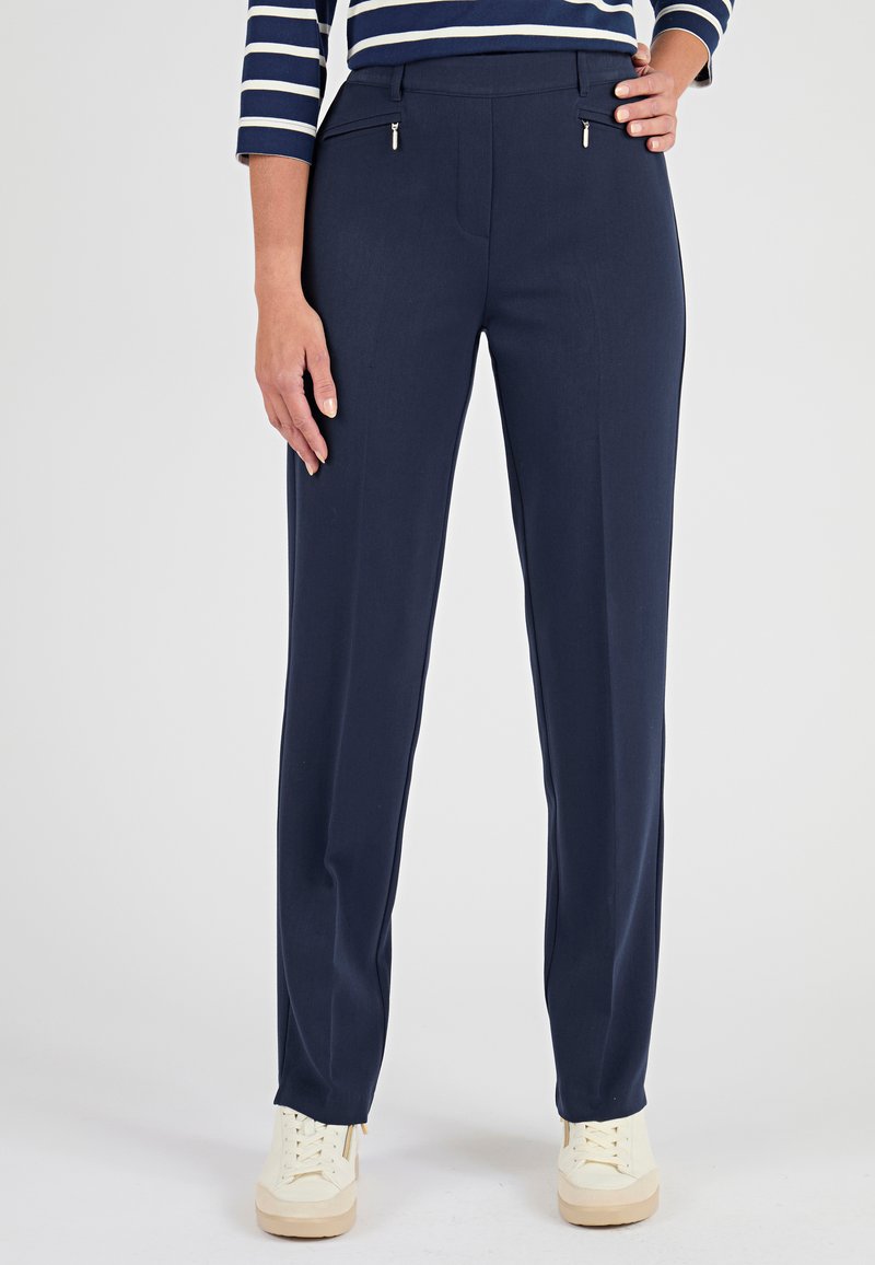 Donna che indossa pantaloni navy a gamba dritta con tasche anteriori con cerniera, abbinati a una maglia a righe a maniche lunghe e sneaker bianche.