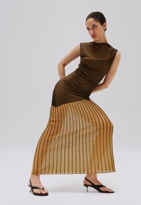 Maxi šaty z priesvitnej tkaniny s hnedo-čiernymi pruhmi, priliehavý živôtik, mierne rozšírený spodok, doplnené čiernymi sandálmi na podpätku.